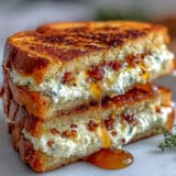 Golden-brown sandwich halves reveal a melting chèvre and cream cheese filling flecked with red pepper flakes and a honey drizzle.