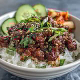 Close-up of Korean Beef Bowl showing glazed ground beef, radish slices, and kimchi on steamed rice.