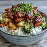 Steaming teriyaki chicken and rice bowl topped with colorful vegetables, scallions, and toasted sesame seeds.