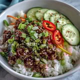 Bright plating of Easy Korean Beef Bowl featuring cauliflower rice, crisp cucumber slices, and julienned carrots topped with sesame seeds.