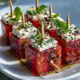 Colorful watermelon feta mint skewers drizzled with olive oil, showcasing vibrant fruit and fresh herbs for a Mediterranean-inspired snack.  