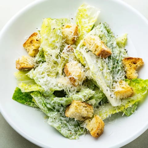 A vibrant bowl of Caesar salad, ready to eat with crunchy croutons and Parmesan cheese.