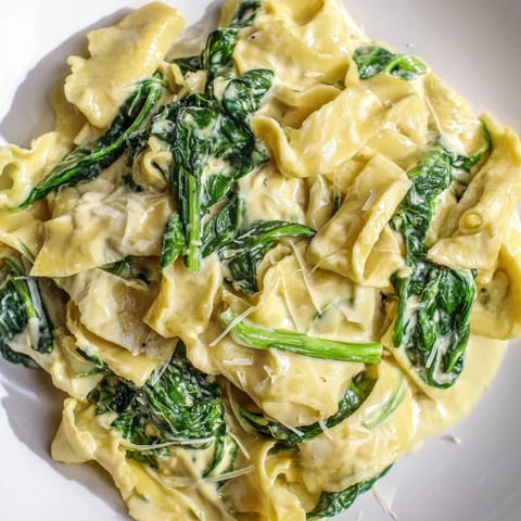 A close-up of Creamy Spinach Garlic Noodles twirled on a fork, showing velvety Parmesan sauce clinging to tender noodles.