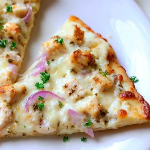 A close-up of a slice being lifted, revealing layers of melted mozzarella, savory chicken, and rich Alfredo on a perfectly baked pizza crust.  