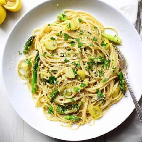 A close-up of roasted garlic and asparagus pasta with golden roasted garlic cloves and bright green asparagus spears tangled in spaghetti.