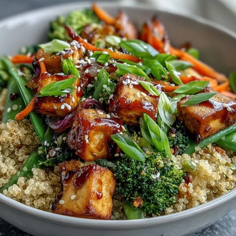 Fluffy quinoa and crispy tofu are tossed with vibrant stir-fried vegetables in a glossy teriyaki sauce inside a ceramic bowl.
