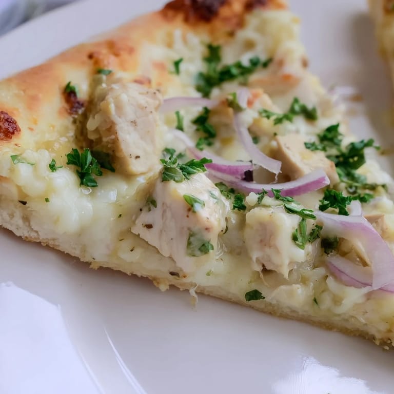 Sliced Chicken Alfredo Pizza on a wooden board, garnished with fresh parsley and a side of marinara for dipping.