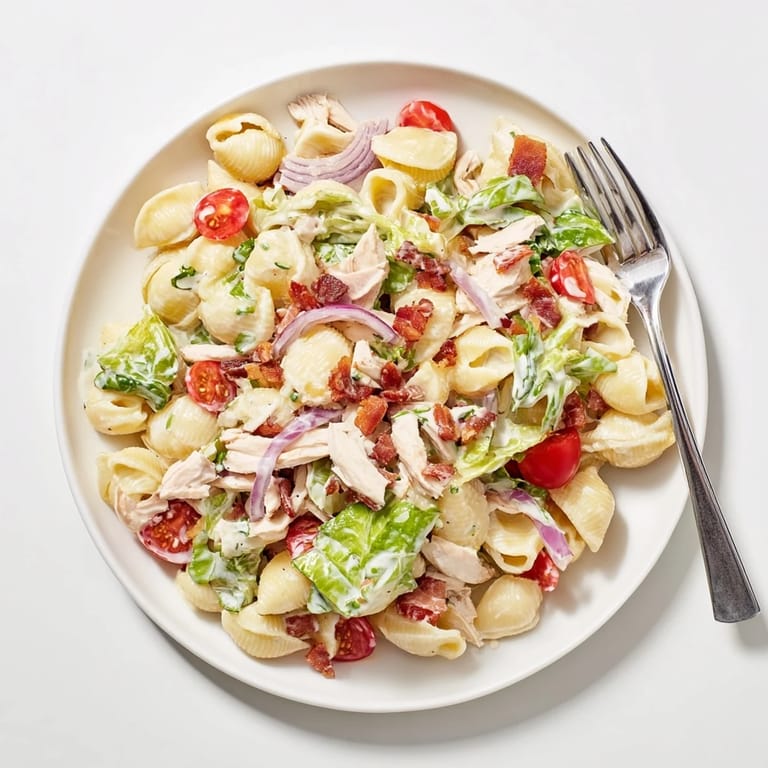 Chilled BLT Chicken Pasta Salad on a picnic table, garnished with herbs and a light mayo-Greek yogurt dressing.