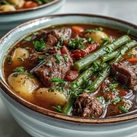 A hearty bowl of Beef and Vegetable Soup garnished with fresh parsley, served beside crusty bread.