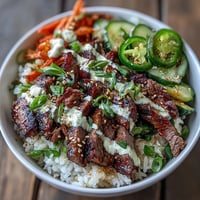 A vibrant Korean Beef Power Bowl with sesame-ginger beef, fluffy rice, pickled carrots, cucumber, and spicy sriracha mayo.
