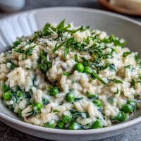 Creamy spring pea and mint risotto with Parmesan, garnished with fresh herbs and lemon zest for a vibrant vegetarian dinner.